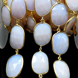 May include: A strand of white opal gemstone beads with gold-toned connectors. The beads are oval-shaped and have a faceted finish.