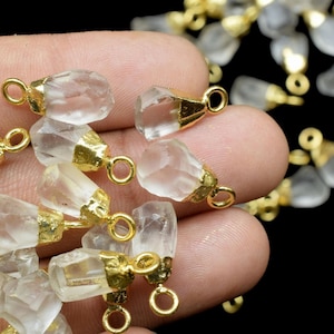 Può includere: Una collezione di ciondoli in cristallo di quarzo trasparente con anelli a salto placcati in oro. I ciondoli sono sfaccettati e hanno un aspetto naturale e grezzo.