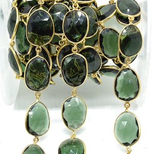 May include: A strand of green gemstone beads with gold-colored metal settings. The gemstones are oval-shaped and faceted, with a deep green color. The beads are connected by small gold-colored links, creating a chain.