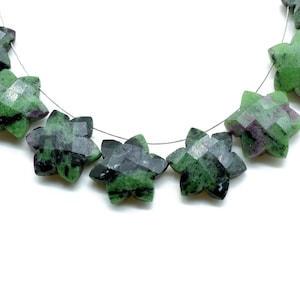 Könnte beinhalten: Eine Kette aus sternförmigen Edelsteinen in Grün, Schwarz und Pink. Die Perlen sind facettiert und auf einem Silberdraht aufgefädelt.