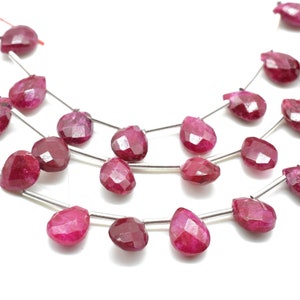Könnte beinhalten: Eine Strähne aus rubinroten Edelsteinperlen in facettiert tropfenförmiger Form. Die Perlen sind auf Silberdraht aufgefädelt.