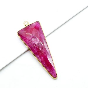 May include: A gold-toned pendant featuring a triangular shaped pink gemstone with a faceted design.