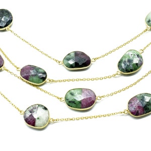 以下が含まれることがあります： ゴールドチェーンと楕円形の緑とピンクの宝石が付いたマルチストランドネックレスです。