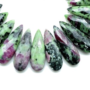 May include: A strand of green, pink and black gemstone beads in a teardrop shape.