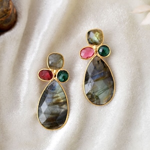 Puede incluir: Un par de pendientes en forma de lágrima con engaste de oro. Cada pendiente presenta una piedra grande de labradorita iridiscente y tres piedras más pequeñas: una rosa y dos verdes.