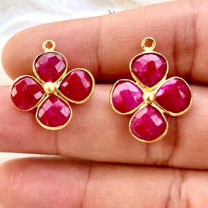 May include: Two gold-tone flower charms with red gemstone accents. Each charm features four red gemstones in a flower shape with a gold-tone center.