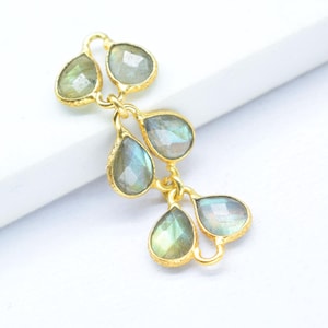 Pode incluir: Uma corrente de ouro com cinco pedras preciosas de labradorita em forma de lágrima. As pedras preciosas são de cor azul esverdeada clara com um efeito iridescente brilhante.