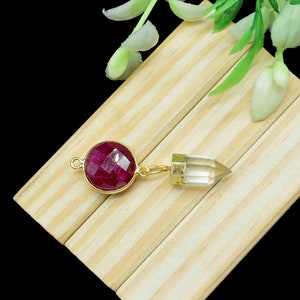 Puede incluir: Una cadena de oro con un colgante de piedra roja y un colgante de cristal de cuarzo transparente.