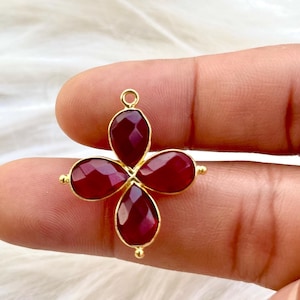 May include: A gold pendant with a four-leaf clover design featuring red gemstone accents.