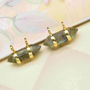 Pode incluir: Dois pingentes de charme banhados a ouro com uma pedra de labradorita verde facetada com ponta. Cada charme tem dois laços dourados para prender a um colar ou pulseira.