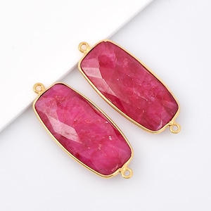 Puede incluir: Dos colgantes rectangulares de piedra preciosa roja rubí con engastes de metal dorado y anillas de salto.