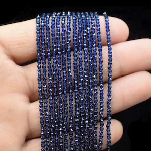 Peut inclure: Un brin de perles de pierres précieuses facettées bleu foncé. Les perles sont petites et rondes, et elles sont enfilées sur un fil transparent. Le brin mesure environ 46 cm de long.