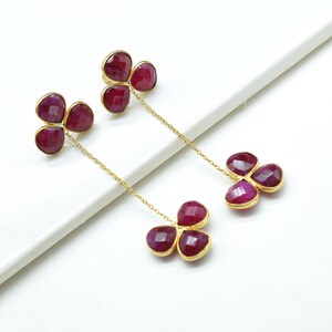 Pode incluir: Um par de brincos de ouro com três pedras de cor rubi em cada brinco. As pedras são conectadas por uma corrente de ouro.