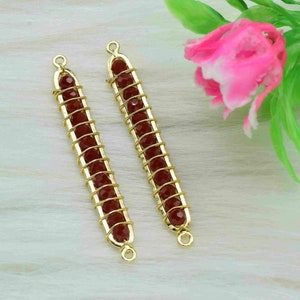 May include: Two gold-colored, rectangular jewelry components. Each features a row of red-brown beads encased in a gold wire cage. The ends have small loops for attachment. The background includes a pink flower and white fur.