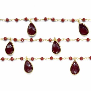 以下が含まれることがあります： 小さな赤いビーズの複数の鎖と、赤い宝石の雫型のペンダントがぶら下がった、金のチェーンネックレスです。