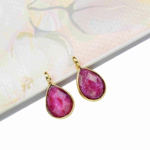May include: Two gold-toned teardrop-shaped pendants with pink gemstone inserts.