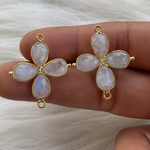 Pode incluir: Dois conectores em forma de flor dourados com quatro pedras de lua branca cada um. Os conectores têm um laço de cada lado para prender em joias.