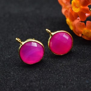 Pode incluir: Um par de brincos dourados com detalhes de pedras preciosas cor-de-rosa. Os brincos têm um formato redondo e um design simples.