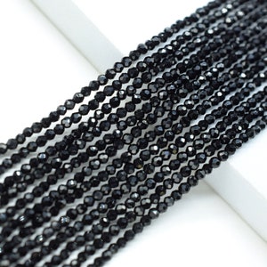 May include: A strand of black faceted gemstone beads. The beads are small and uniform in size, and they are strung on a clear thread.