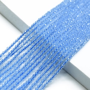 Puede incluir: Una hebra de cuentas de cristal facetadas de color azul claro. Las cuentas son pequeñas y redondas, y están enhebradas en un hilo transparente.