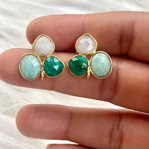 Puede incluir: Un par de pendientes de oro con tres gotas de piedras preciosas. Los pendientes presentan una piedra preciosa blanca en la parte superior, seguida de una piedra preciosa verde claro y una piedra preciosa verde oscuro en la parte inferior.