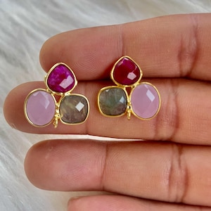 Könnte beinhalten: Ein Paar goldene Ohrringe mit drei Edelstein-Akzenten. Die Ohrringe haben einen rosa, einen grünen und einen roten Edelstein.