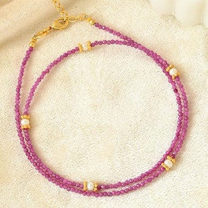 May include: A delicate gold chain necklace with two strands of pink beads and white pearl accents.