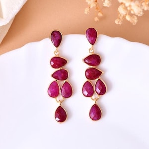 May include: A pair of dangle earrings with a gold setting and five teardrop-shaped ruby red stones.