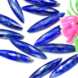 Könnte beinhalten: Eine Sammlung von zwölf facettierten, dunkelblauen Lapislazuli-Edelstein-Spitzen, die auf einer weißen Oberfläche angeordnet sind. Die Spitzen sind alle ungefähr gleich groß und geformt und haben eine glänzende, polierte Oberfläche.