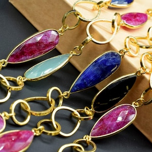 以下が含まれることがあります： ピンク、ブルー、グリーン、ブラックなど、さまざまな色の涙型の宝石がついたゴールドチェーンネックレスです。