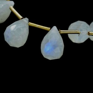 Puede incluir: Una hebra de cuentas de piedra lunar iridiscente enhebradas en alambre dorado. Las cuentas son facetadas y tienen forma de l&aacute;grima.