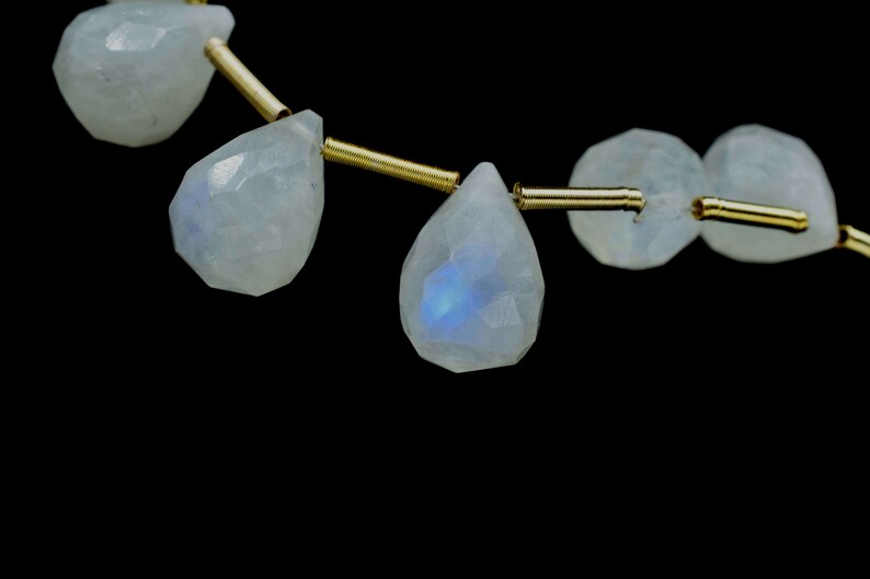 Puede incluir: Una hebra de cuentas de piedra lunar iridiscente enhebradas en alambre dorado. Las cuentas son facetadas y tienen forma de l&aacute;grima.