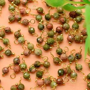 May include: A collection of green, red, and gold gemstone beads with gold jump rings. The beads are faceted and have a natural, organic look.