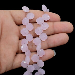 May include: A strand of pale pink gemstone beads, each bead is carved in the shape of a flower. The beads are strung on a silver wire.