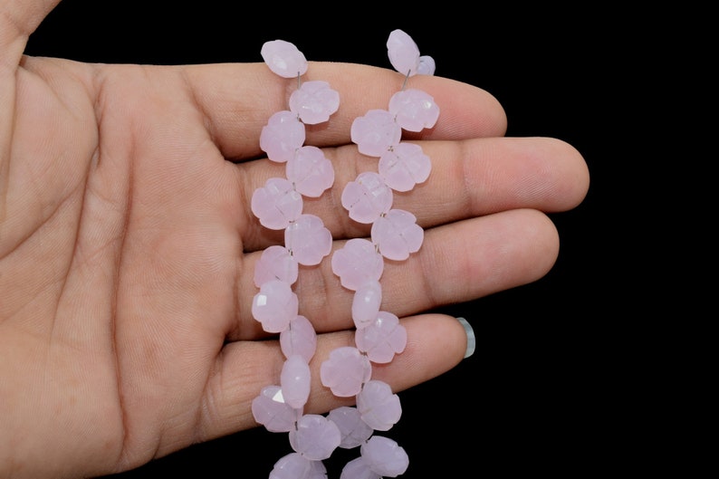 May include: A strand of pale pink gemstone beads, each bead is carved in the shape of a flower. The beads are strung on a silver wire.