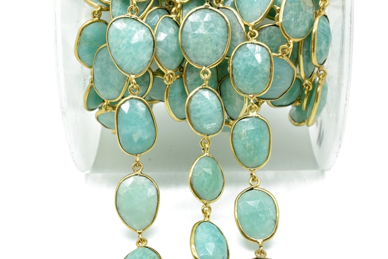 May include: A gold chain with light blue, faceted, oval-shaped gemstones. The chain is wound around a spool.