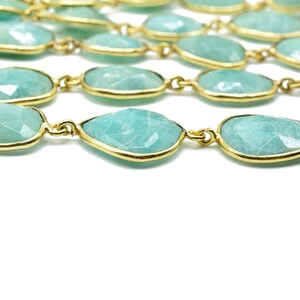 May include: A strand of light green gemstone beads with gold accents. The beads are faceted and have a teardrop shape.