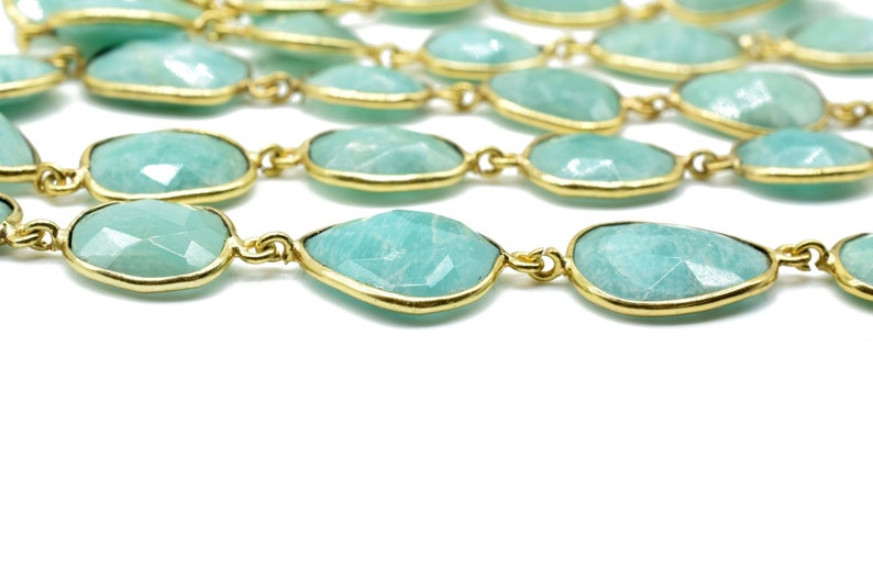 May include: A strand of light green gemstone beads with gold accents. The beads are faceted and have a teardrop shape.