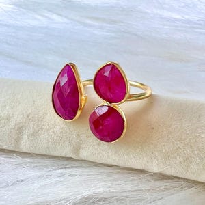 May include: A gold ring with two pink gemstone accents. The ring is designed to be worn on the knuckle.