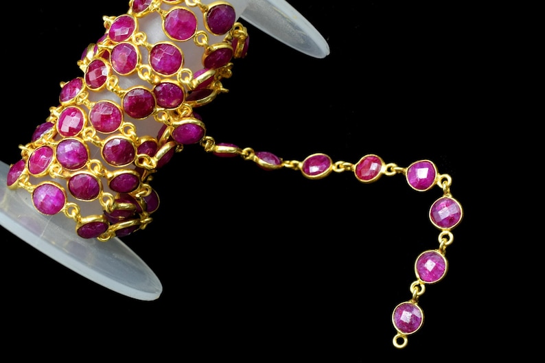 May include: A spool of gold chain with pink gemstone beads. The chain is made of small, round links and the beads are faceted and have a shiny finish.