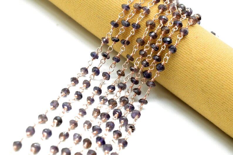 May include: A strand of dark purple gemstone beads strung on a rose gold chain. The beads are faceted and have a slightly irregular shape.