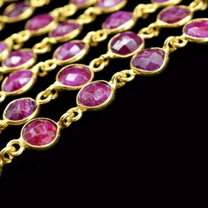May include: A close-up of a gold chain with multiple strands of pink gemstones. The chain is on a black background.