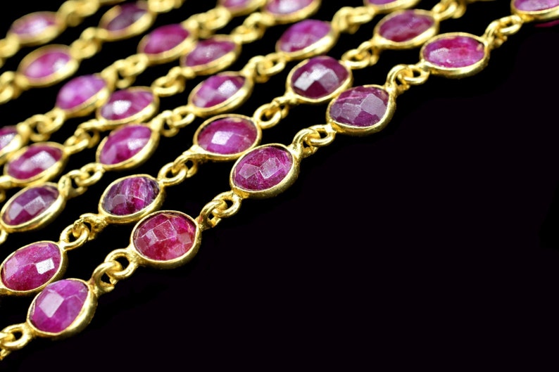 May include: A close-up of a gold chain with multiple strands of pink gemstones. The chain is on a black background.