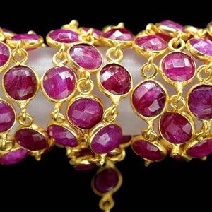 May include: A strand of gold chain with faceted ruby red gemstone beads. The chain is made of small, round links and the beads are approximately 1.2 cm in diameter.