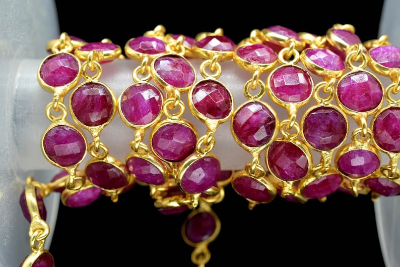 May include: A strand of gold chain with faceted ruby red gemstone beads. The chain is made of small, round links and the beads are approximately 1.2 cm in diameter.