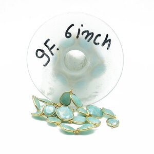 May include: A strand of light blue gemstone beads with gold accents. The beads are approximately 15 cm long and are displayed on a clear glass surface with the text "6 inch" and "gf." written on it.