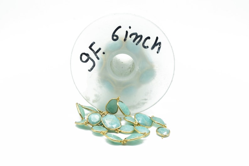 May include: A strand of light blue gemstone beads with gold accents. The beads are approximately 15 cm long and are displayed on a clear glass surface with the text "6 inch" and "gf." written on it.