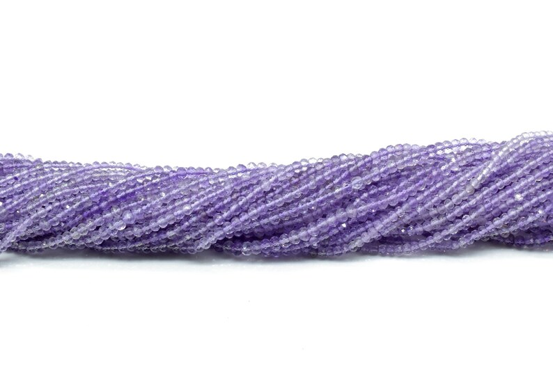 May include: A strand of light purple amethyst beads. The beads are faceted and have a slightly irregular shape. The beads are strung on a clear thread.