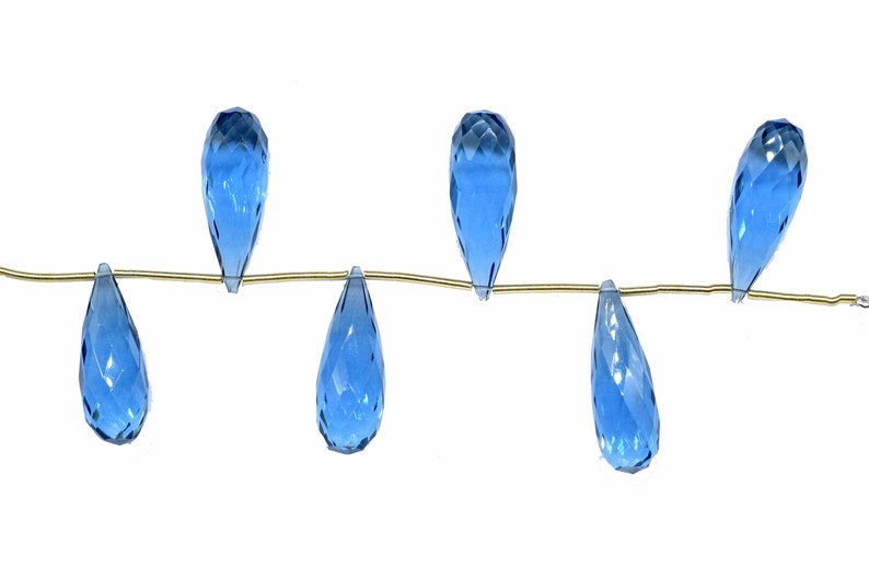 May include: A strand of six teardrop-shaped blue topaz beads strung on a gold wire.