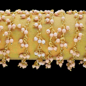 Könnte beinhalten: Eine goldene Kette mit rosa Perlen, die daran hängen. Die Kette besteht aus kleinen, filigranen Gliedern und die Perlen sind gleichmäßig verteilt.